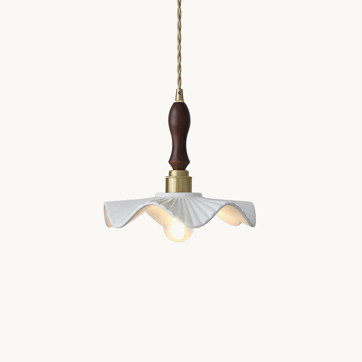 White wavy-edged ceramic shade under a brass socket and a dark carved wooden handle, this Clérachic pendant on a twisted cord against white.