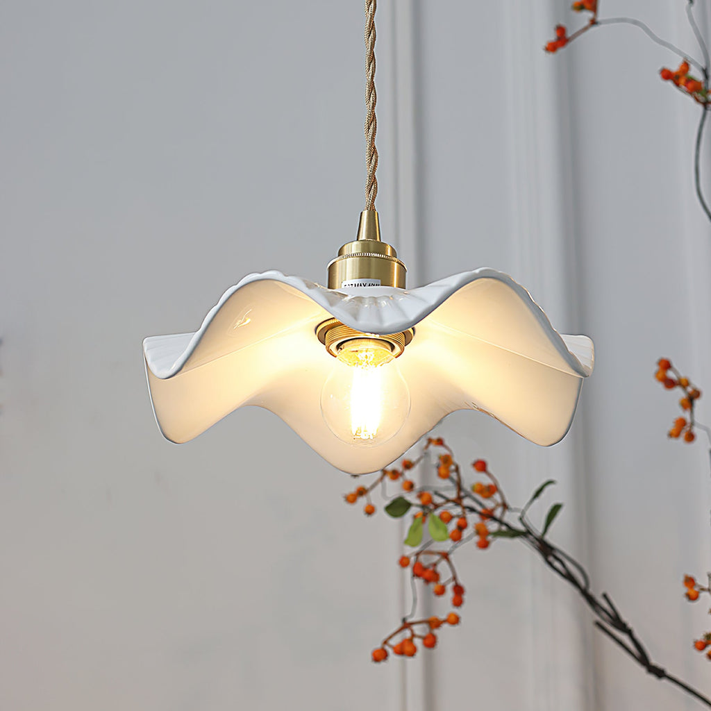 Warm bulb glowing inside the rippled white ceramic shade of this Clérachic pendant, with a branch of orange berries behind it.