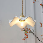 Warm bulb glowing inside the rippled white ceramic shade of this Clérachic pendant, with a branch of orange berries behind it.