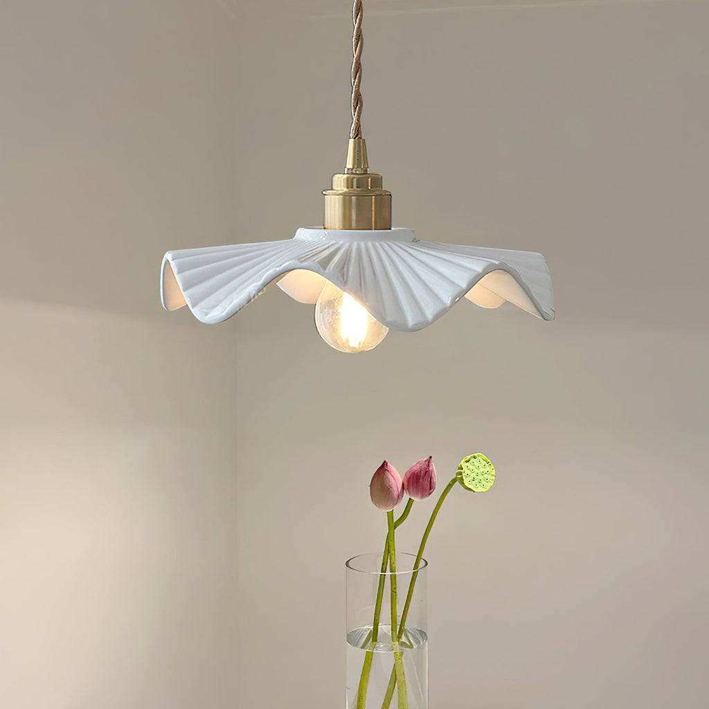 Pleated white ceramic shade with a brass cap on a twisted cord, this Clérachic pendant beside a vase of pink lotus stems.