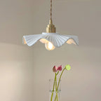 Pleated white ceramic shade with a brass cap on a twisted cord, this Clérachic pendant beside a vase of pink lotus stems.