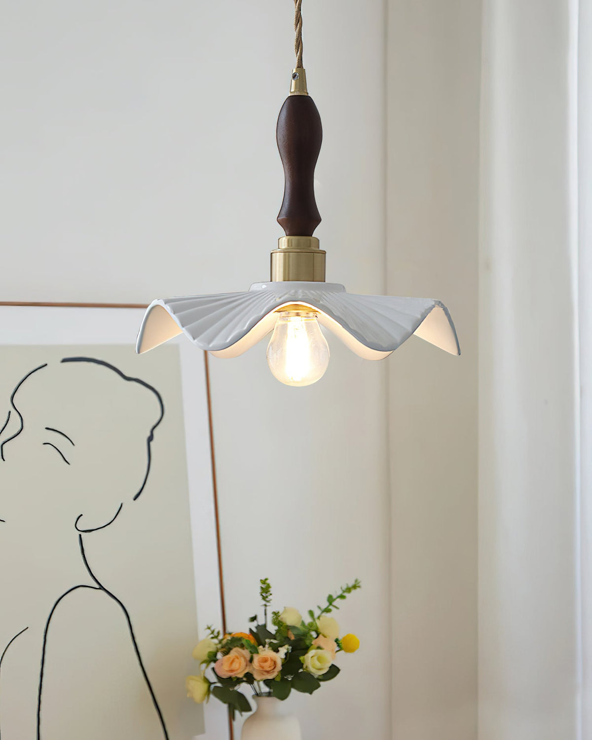 This Clérachic pendant hangs in front of a line-drawing portrait and a posy of yellow flowers, with a dark wooden handle above the brass cap.