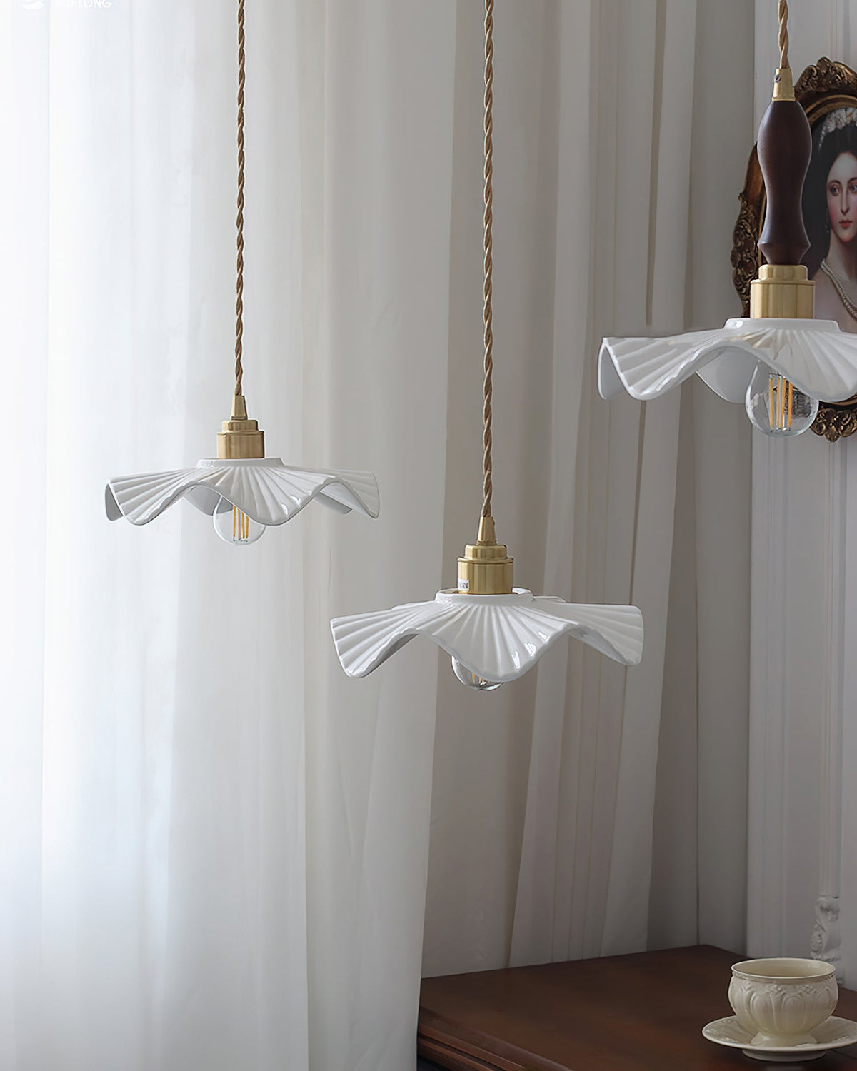 Three of this Clérachic pendant's wavy ceramic shades hang at different heights in front of white curtains.