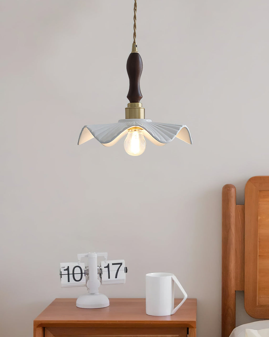 This Clérachic pendant hangs over a small wooden bedside table with a flip clock and a white mug, beside a wooden headboard.