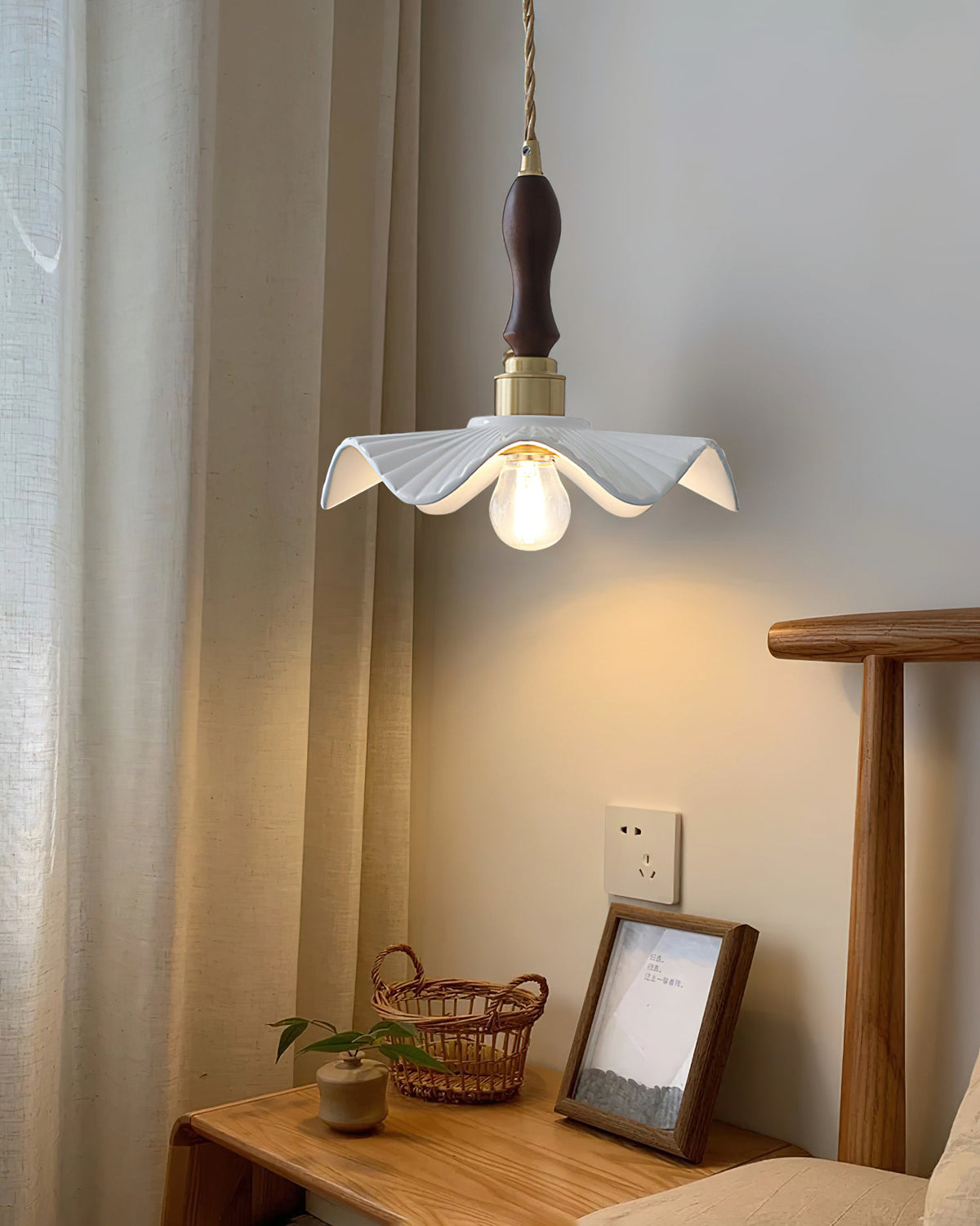 A Clérachic pendant with a dark wooden handle glows warmly beside cream curtains above a wooden desk and a framed picture.