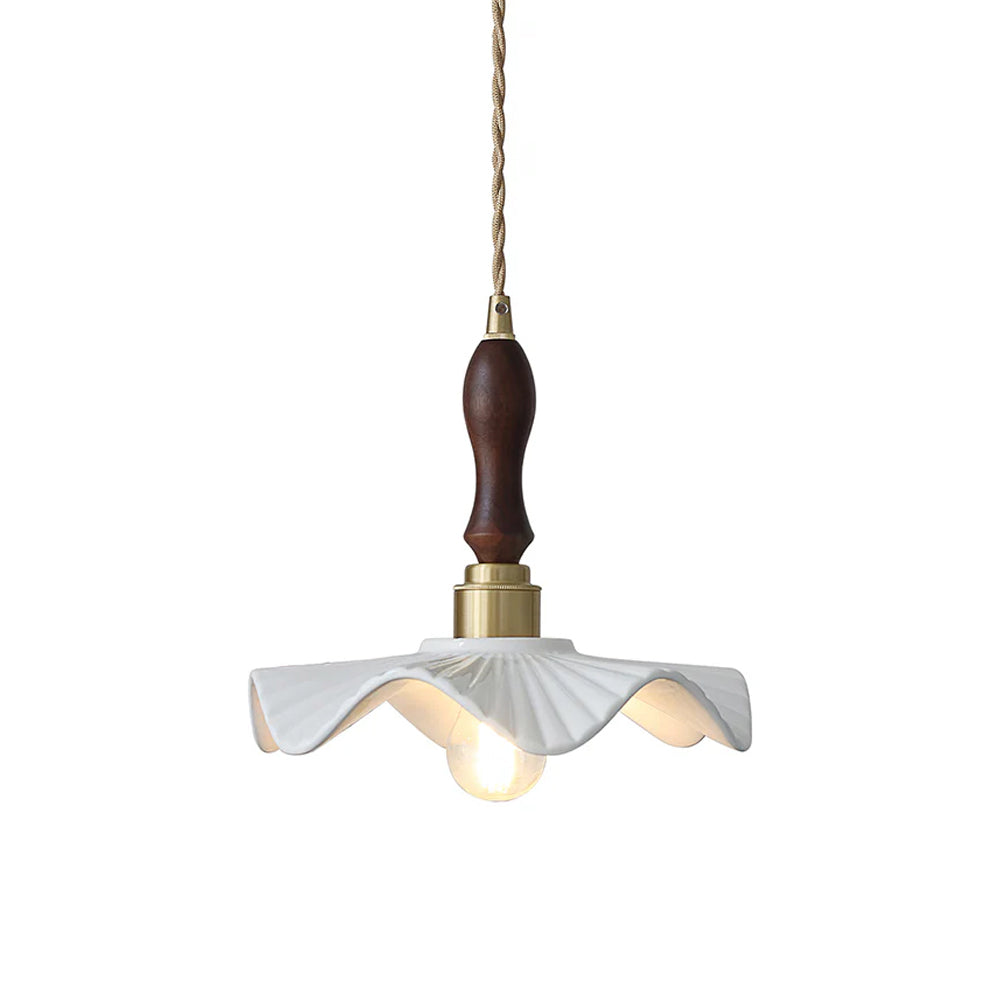 White wavy ceramic shade with a brass socket and a dark wooden handle on a twisted cord, this Clérachic pendant on a white backdrop.