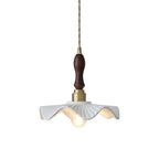 White wavy ceramic shade with a brass socket and a dark wooden handle on a twisted cord, this Clérachic pendant on a white backdrop.