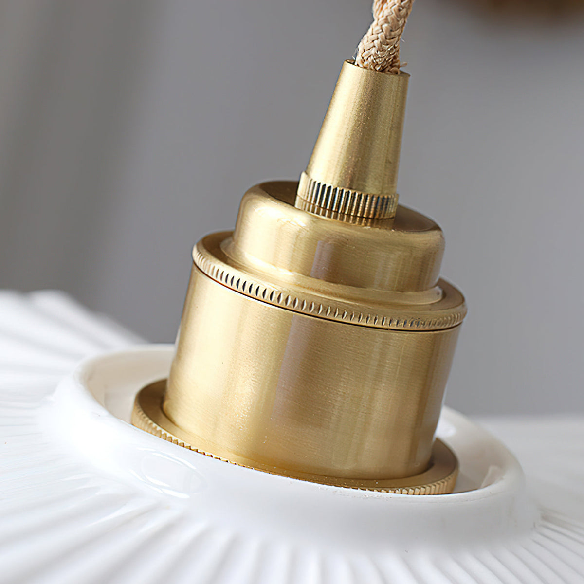 Close view of the brass lamp holder and knurled ring where the twisted cord meets the white ceramic shade of this Clérachic pendant.