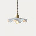 Short Clérachic pendant with a pleated white ceramic shade, a brass cap and a lit filament bulb, against a pale background.