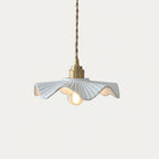 Short Clérachic pendant with a pleated white ceramic shade, a brass cap and a lit filament bulb, against a pale background.