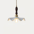 This Clérachic pendant glows softly, with a dark wooden handle above the brass socket and a rippled white shade, on a pale backdrop.