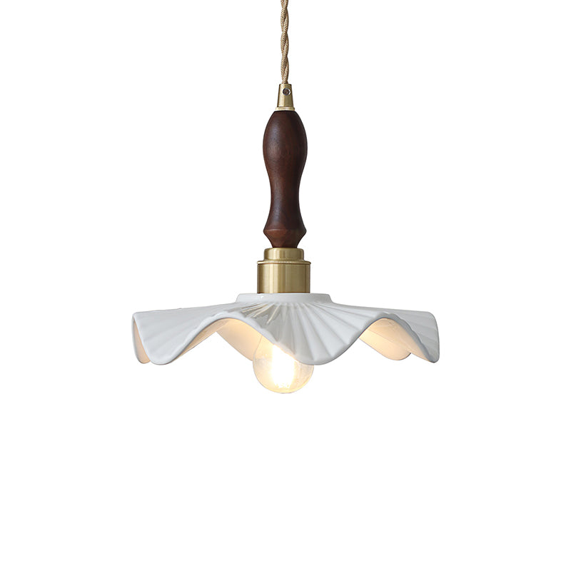 A Clérachic pendant with a dark wooden handle, brass socket and wavy white ceramic shade, seen on a white backdrop.