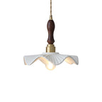 A Clérachic pendant with a dark wooden handle, brass socket and wavy white ceramic shade, seen on a white backdrop.