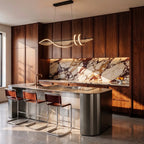 Clérachic black wavy LED pendant glowing above a steel kitchen island with leather stools, walnut cabinets and marble splashback.