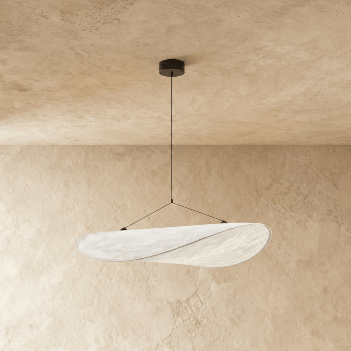 Clérachic twisted white pendant shade glowing softly, hung from a black ceiling rose against a warm limewash plaster wall.