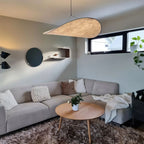 Clérachic leaf-shaped white pendant glowing warmly above a grey corner sofa and round oak coffee table in a living room.