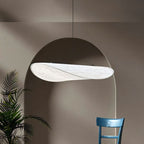 Clérachic white leaf-shaped pendant lit from within, hanging in front of an arched alcove with a palm and a blue chair.