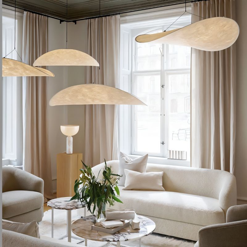 Clérachic cluster of glowing white pendants in different shapes hung at varied heights in a living room with long curtains.