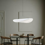 Clérachic white leaf-shaped pendant lit over a round dark dining table with wooden chairs, in a muted grey-green room.