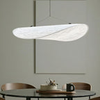 Close view of a Clérachic white pendant over a round marble-top table, showing the soft veined texture of its twisted shade.