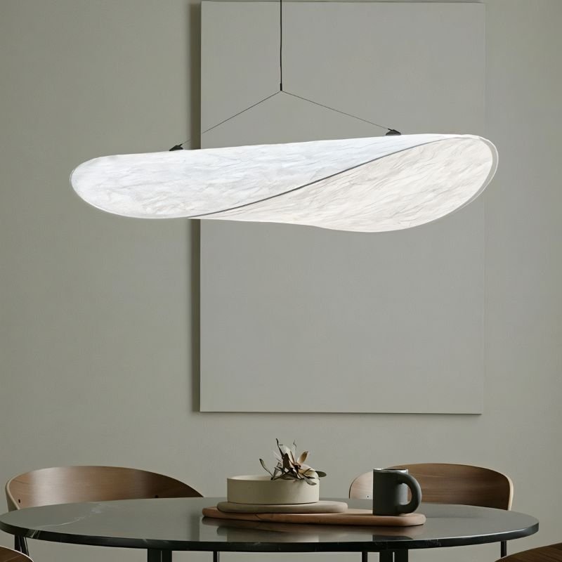 Close view of a Clérachic white pendant over a round marble-top table, showing the soft veined texture of its twisted shade.