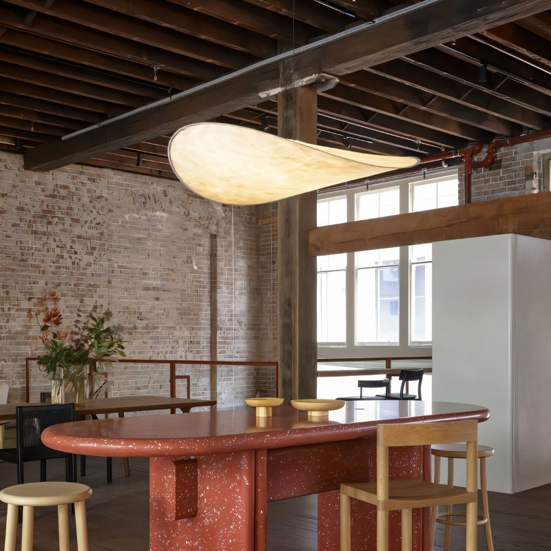 Clérachic large white pendant glowing warm above a red terrazzo counter in a brick loft with exposed timber beams.
