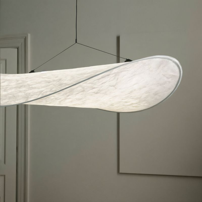 Close view of a Clérachic white pendant shade, its folded edge and fine fibre texture glowing softly against a grey wall.