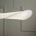 Close view of a Clérachic white pendant shade, its folded edge and fine fibre texture glowing softly against a grey wall.