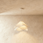 Clérachic pendant with soft rippled white fabric layers glowing warmly, hung from a white canopy against plaster.