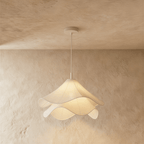 Clérachic layered white fabric pendant lit from within, its wavy edges casting a warm glow on a limewash wall.