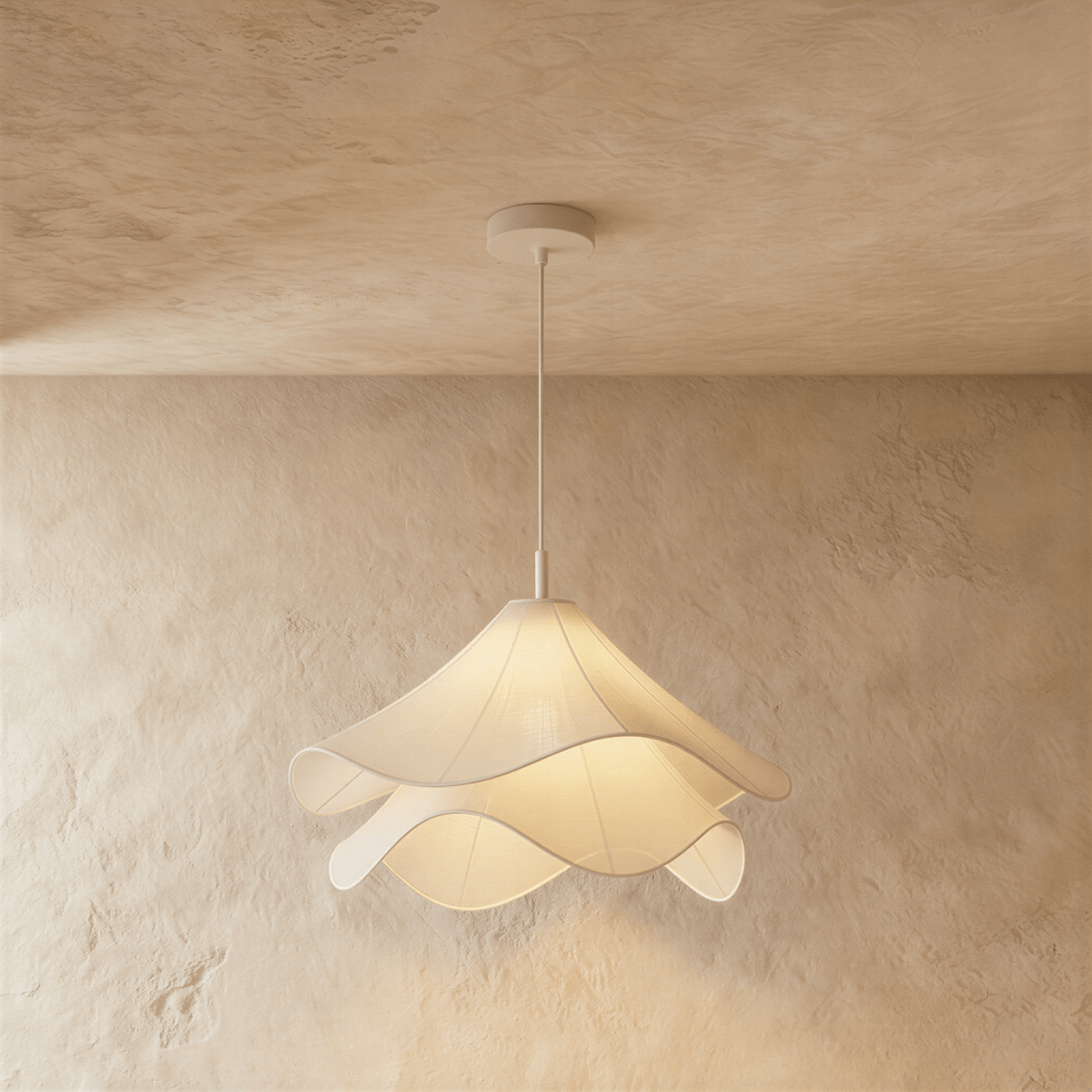 Clérachic layered white fabric pendant lit from within, its wavy edges casting a warm glow on a limewash wall.