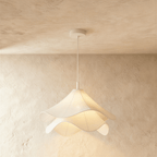 Clérachic wave-edged fabric pendant seen close up, two tiers of white cloth diffusing warm light below a white canopy.