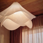 Close view of a Clérachic fabric pendant, its stitched ribs and rippled white layers glowing against wood and curtains.