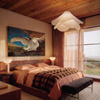Clérachic white fabric pendant with rippled layers above a bed, with timber ceiling, rust curtains and a large painting.