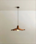 Clérachic pendant with a wavy, walnut-toned wooden shade on a slim dark cord, lit by a frosted globe bulb, studio shot.
