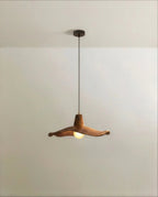 Clérachic pendant with a wavy, walnut-toned wooden shade on a slim dark cord, lit by a frosted globe bulb, studio shot.