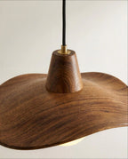 Close up of the Clérachic pendant: a tapered walnut-grain cap with a brass fitting on a black fabric cord above the wave shade.