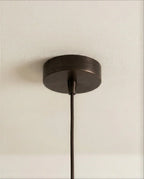 Clérachic pendant detail of the round dark bronze ceiling canopy and braided cord against a pale ceiling.
