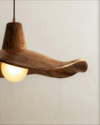 Clérachic pendant close up showing the curled wooden rim, fine grain and the glowing frosted globe bulb under the shade.