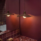 Clérachic wavy wooden pendants and their reflection in a mirror, casting warm light across a deep burgundy wall in a room.