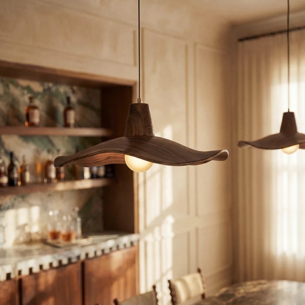 Clérachic wavy wooden pendant glowing over a dining room with a marble-top table, wood chairs and a stone-backed shelf.