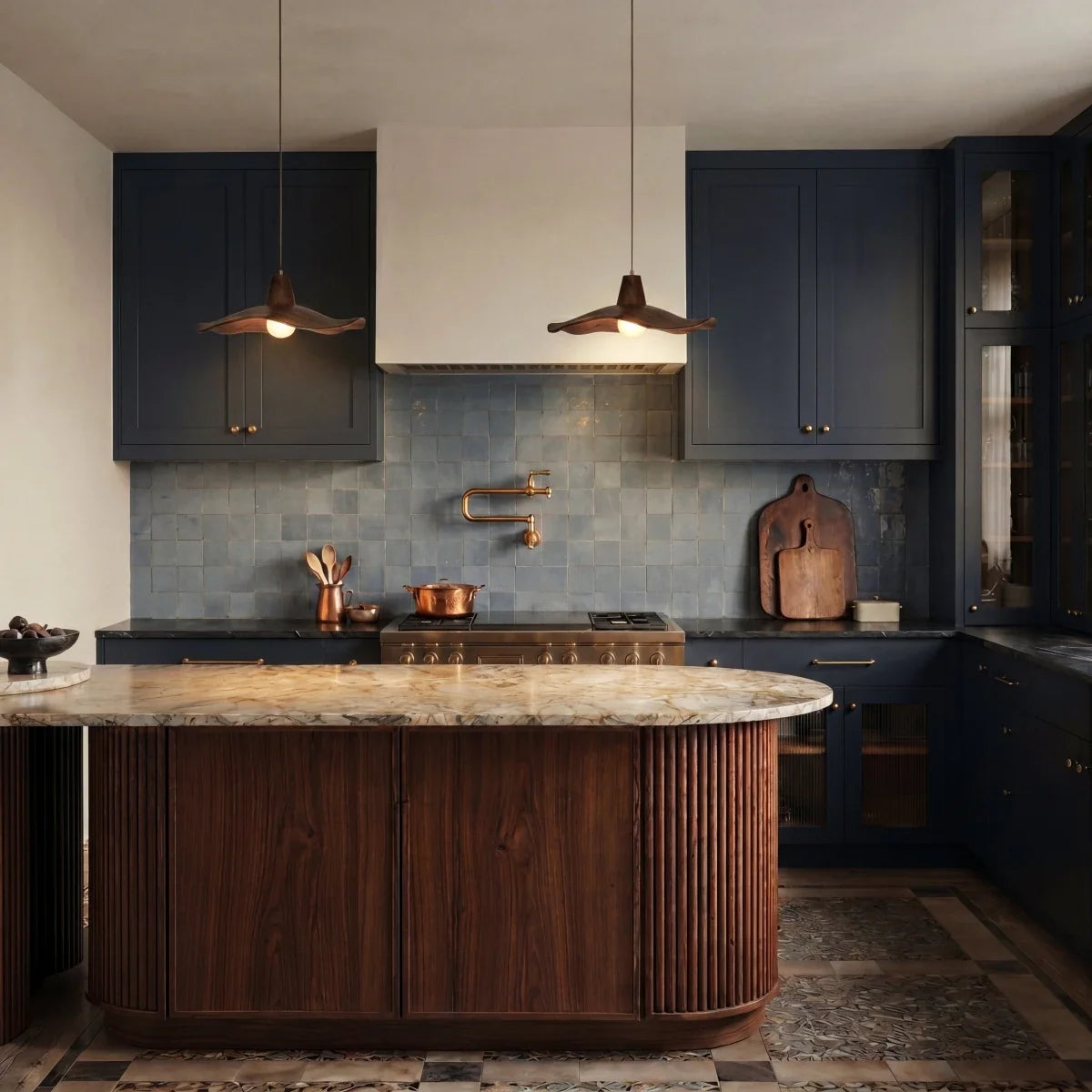Clérachic pair of wavy wooden pendants hanging above a curved wood kitchen island with navy cabinets and blue tile.