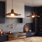 Clérachic wooden pendants softly blurred in the foreground of a kitchen room with navy cabinets and a gleaming pot filler.