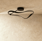Clérachic black curved ceiling light switched off, showing the matt aluminium band and pale diffuser strip on a plaster ceiling.