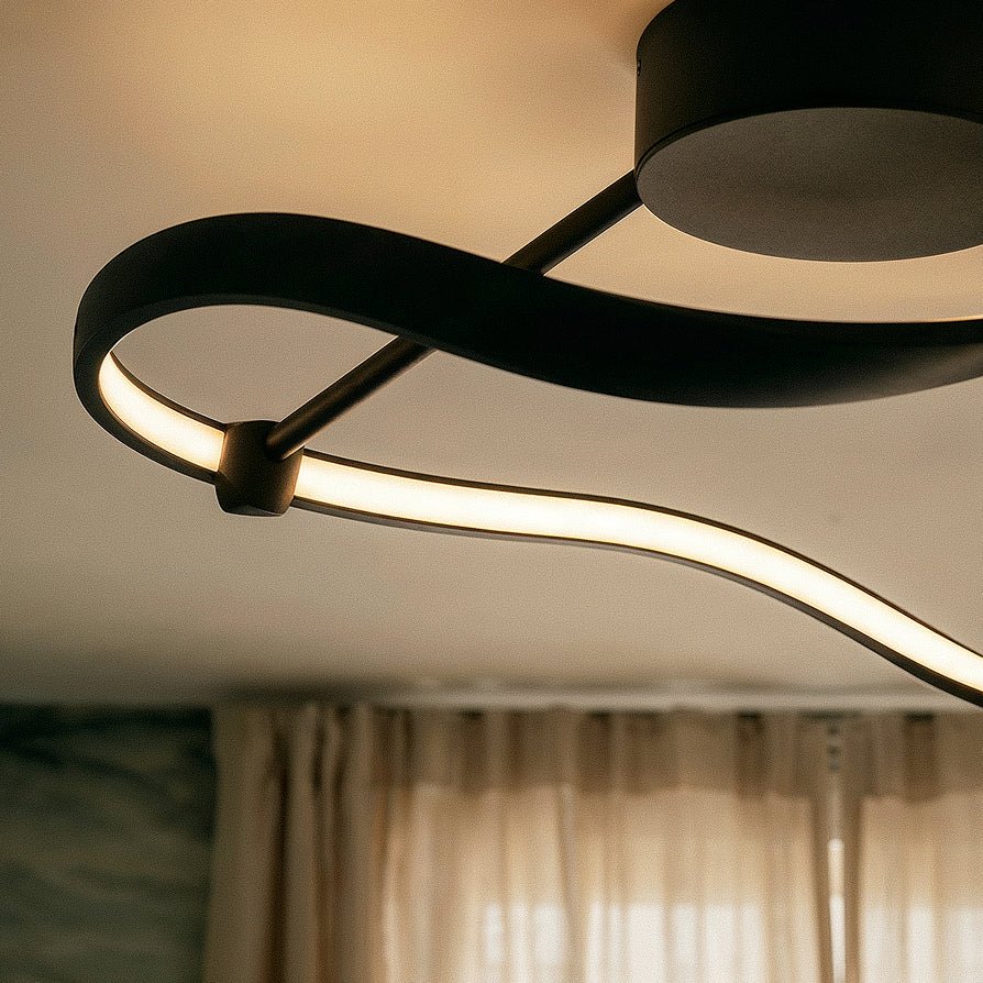 Close view of the Clérachic black ribbon light, showing the matt aluminium band, round joint, slim arm and warm LED strip.