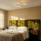 Clérachic white ribbon ceiling light glowing over a bedroom with an olive velvet headboard, linen bedding and low morning sun.