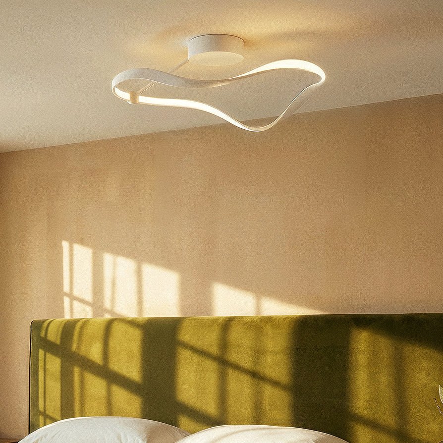 Clérachic white ribbon ceiling light seen from below, casting a soft glow over an olive headboard and a sunlit wall.