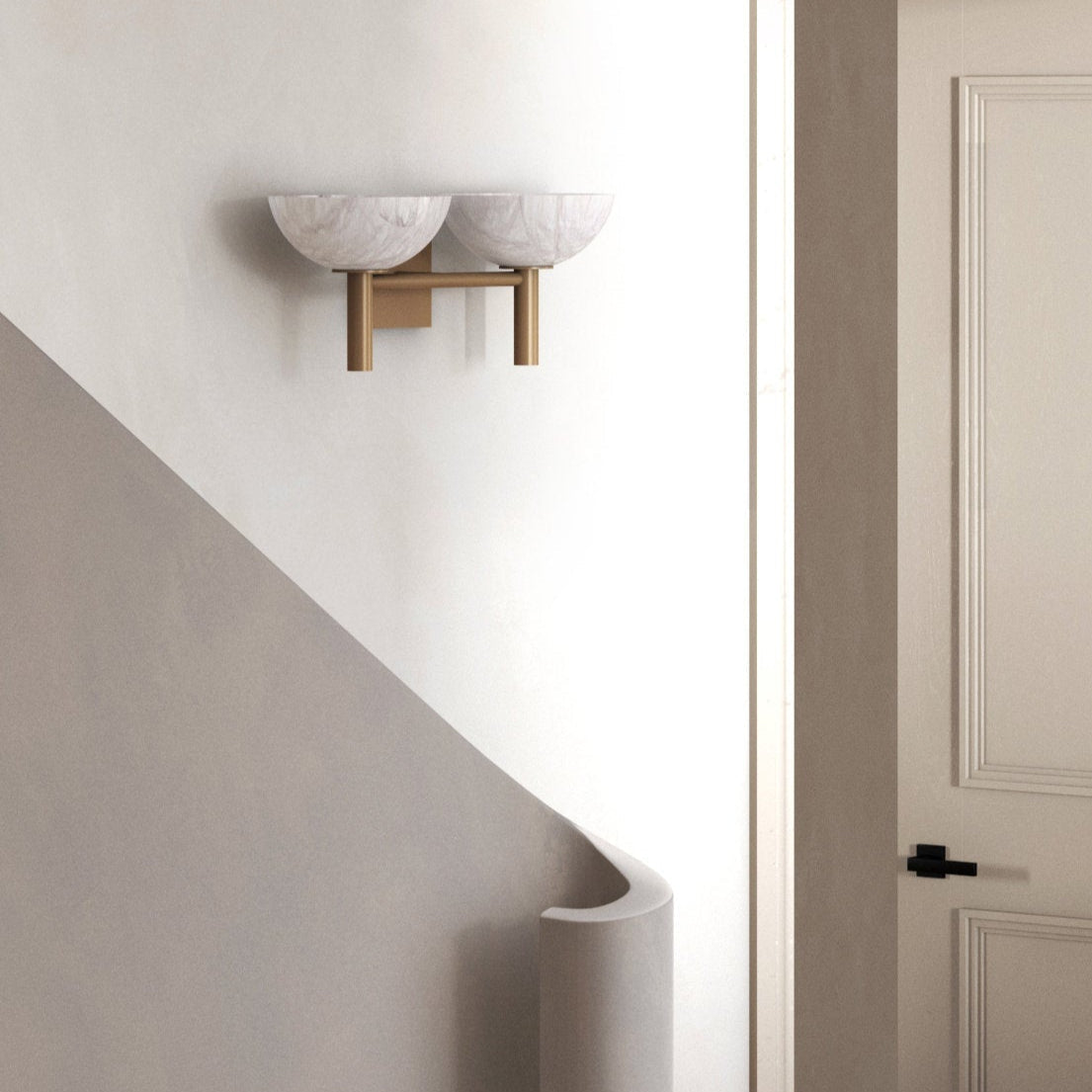 The Clérachic Weft sconce in brass mounted above a curved staircase, sitting flush against the plaster.