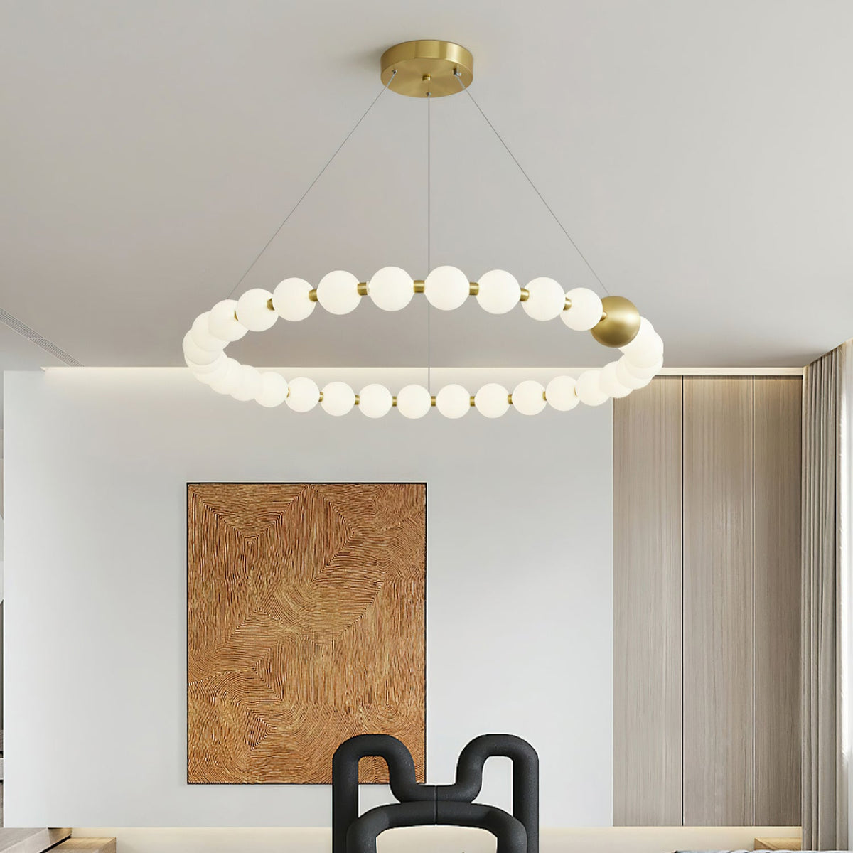 A single ring of white globes with one brass sphere hangs in a Clérachic chandelier, above a dining space with a copper-toned artwork.