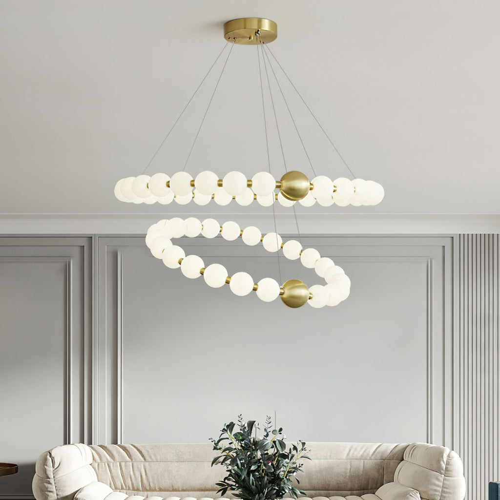 Above a cream boucle sofa and a potted plant, this Clérachic chandelier has two offset rings of lit white globes on brass fittings.